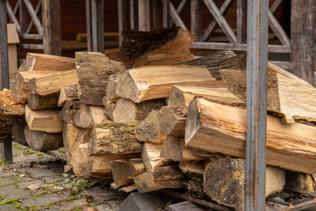 Chopped firewood lies stacked next to a wooden shelter, prepared for winter use in a calm outdoor...