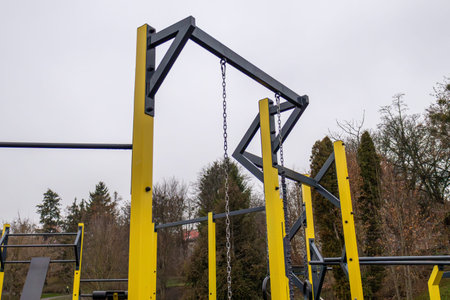 Fitness equipment stands in a park setting. The area has yellow and black structures. Trees are...