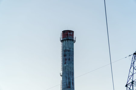 The towering chimney rises sharply into a serene evening sky, surrounded by industrial structures,...