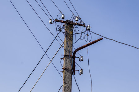 An electric pole is positioned under a clear blue sky, with multiple wires attached and extending in...