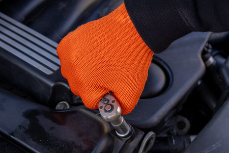 A mechanic works on an engine using a wrench to tighten a bolt while wearing an orange glove in a...