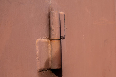The image shows a close view of a red metal gate hinge with some rust next to a wooden fence in an urban setting during daytime.の写真素材