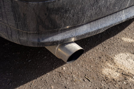 A close view of a car exhaust pipe with dirt buildup on a sunny day in a suburban area. The exhaust...