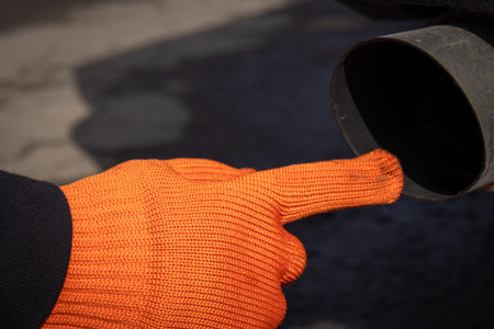 A man points his finger at the exhaust pipe while checking the vehicle in a garage during the day.
