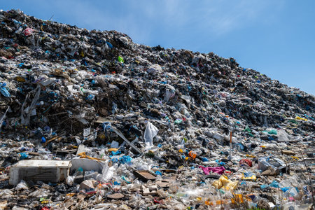 Large pile of trash sits under blue sky, showing various types of waste including plastics, papers, and other items strewn about.