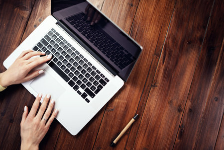 Closeup photo of female hands with a laptop on wooden table. Female freelancer connecting to internet via computer. Blogger or journalist writing new article.の写真素材