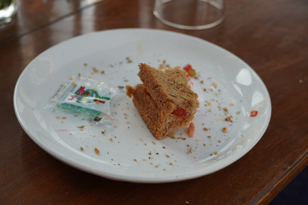 Last bite of a vegetable sandwich kept on plate. Side view shot of a piece bread with tomato with...