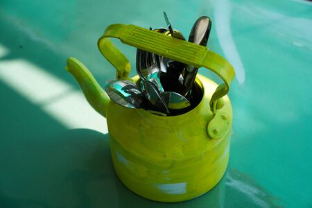 Kitchen utensils and cutlery in old fashioned green vintage teapot in bucket on table along with pepper shaker. Vintage Whistling kettle on green table.の写真素材