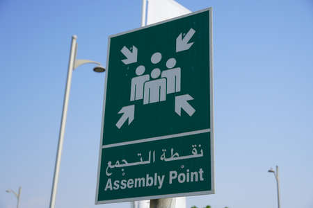 Emergency assembly point information sign in white paint on green background fixed to a pole to direct people where to go in case of an emergency.の写真素材