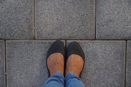 Women Black casual shoes standing and resting on asphalt concrete floor with square tiles. Top View....