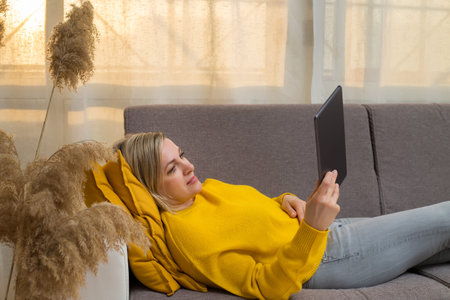 Caucasian woman relaxing on sofa at home using tablet reading and viewing news. Womens relaxing on...