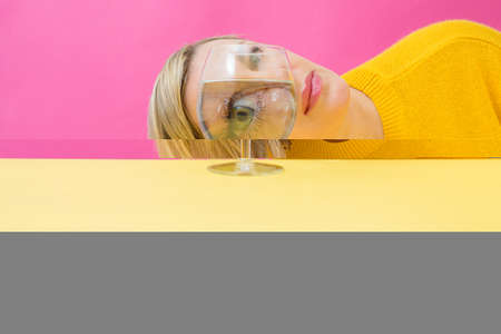 Fashion woman portrait, eye looks through the glass of water. Object distortion, optical illusion. Minimalistic contemporary art.Beautiful womans face in wine glass.Visual concept.の写真素材