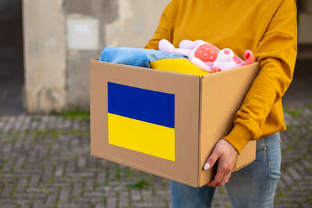 Volunteers hold in their hands a box of humanitarian aid with things and childrens toys for the needs of Ukrainians on the street. Help for Ukraine.Close upの写真素材
