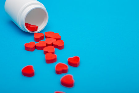 Red heart shaped pills with plastic bottle on blue background.Concept love addiction, love drugs, Valentines Day and depressionの写真素材