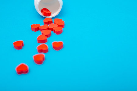 Red heart shaped pills with plastic bottle on blue background.Concept love addiction, love drugs,...
