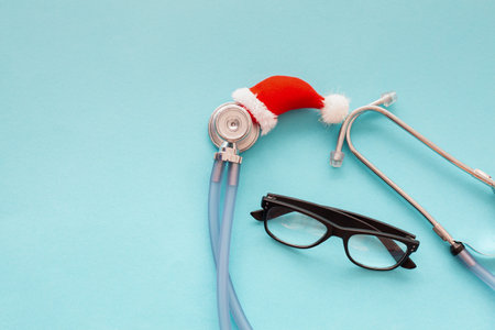Medical stethoscope in a red Santa hat with glasses for vision on a blue background. Creative medical winter background, postcard.の写真素材