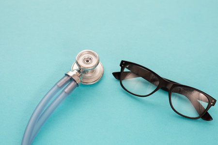 Medical blu stethoscope and black spectacles on blu background. Simply minimal design with medicine equipment Doctor stethoscope and classic glasses, closeup. Health care concept.の写真素材