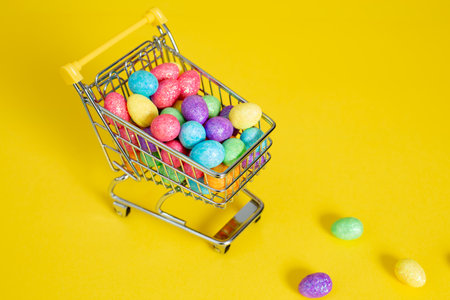 Happy easter.Shopping cart with colorful glitter easter eggs on the yellow background.Top view. High-quality photoの写真素材