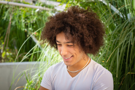 Smiling young ethnic guy 20 years old, dressed in casual clothes, works on a laptop outdoors, in a green area in nature. Green open space for coworking, freelancer, relaxing, coffee, food. Free place to work, business, study, freelance in natureの写真素材