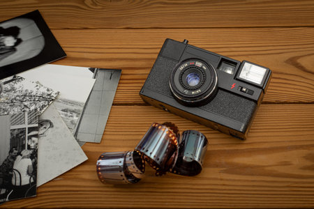 35mm film camera with film negative and black and white photos on wooden background. Old film...