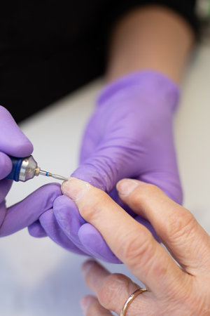 A beautician uses a modern professional electric manicure and pedicure machine to file an elderly womans nails. Various steps to achieve a perfect andの写真素材
