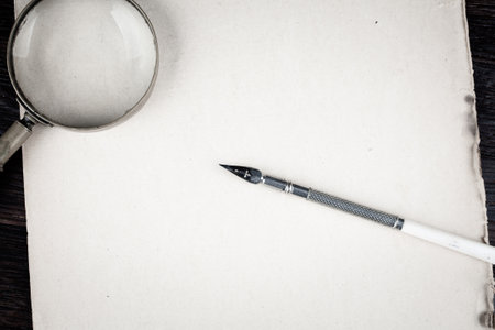 Magnifying glass with old ink feather pen on paper backgroundの写真素材