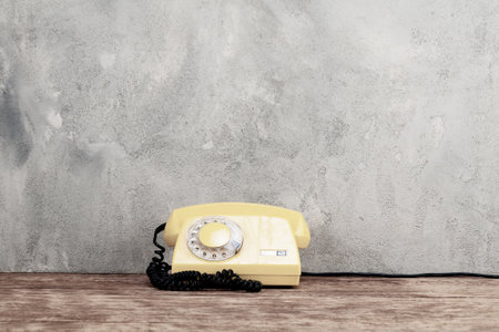 Vintage yellow rotary dial telephone on wooden table in front gray concrete backgroundの写真素材