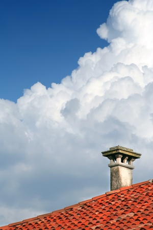a chimney on a roof of a house with blue sky covered with cloudsの写真素材