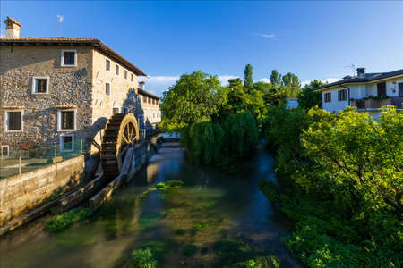 Ancient paddle mill on the river in the medieval village of Strassoldo. Italy. One of the most beautiful villages in Italy. Spontaneous vegetation.の写真素材