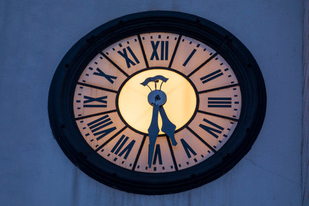 Large illuminated clock, with Roman numerals, of an ancient white bell tower. Night photography.の写真素材