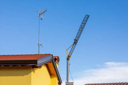 Crane for lifting construction materials over the roof of renovated houses with antenna for receiving television programs. Summer day with clear sky.の写真素材