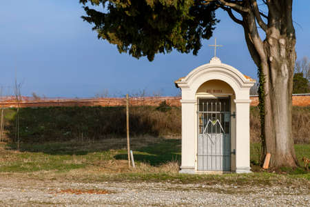 Votive capital small Christian religious architectural structure in the countryside, next to a large tree.の写真素材