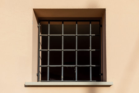 Square window with bars on the facade of an ancient house in the historic center of the old city.