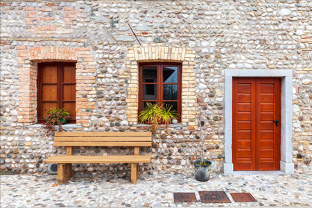 Facade of an old stone and brick house renovated with windows and closed brown wooden door. Wooden quay and flowers in the windows.の写真素材
