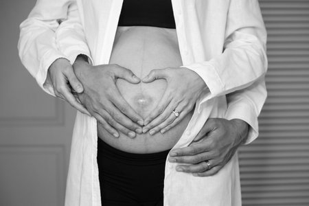 Heart shaped hands over a belly of pregnancy, hand of a man and a women, Black and White