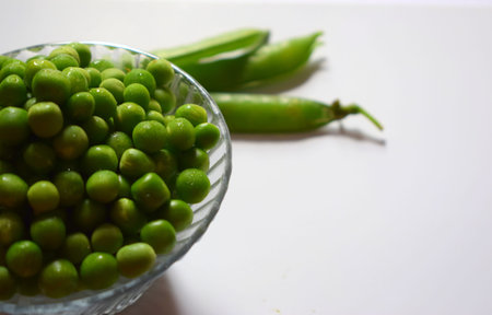 Bowl full of green pead on white and peas' leaf background, with copyspaceの写真素材