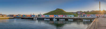 Hummerbuden typical colorful houses at evening on the shore on the island of Helgoland, Schleswig-Holstein, Germany. Panorama view of lobster stalls and harbor with sun flair.の写真素材