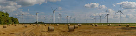 Panorama view of beautiful countryside scene with mowed wheat field, straw bales and wind turbines. Rural landscape with straw bales after harvesting wheat on the field and windmills.の写真素材