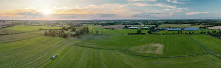 Sunny panorama of rural idyll with agricultural factory, fields, and tractor with slurry tanker by the work in the countryside. Magical country landscape in autumn.の写真素材