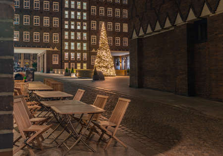 Chilehaus in the Kontorhaus quarter with Christmas tree, Hamburg, Germany. Advent time by Chilehaus in Hamburg at Corona time. Chairs in front of tables in an outdoor cafe.の写真素材