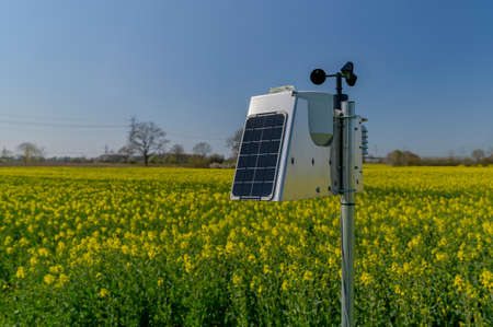 Smart agriculture and smart farm technology. Meteorological instrument used to measure the wind speed and solar cell system in the rape field. Weather station with solar panel placed in the field.の写真素材