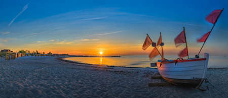 Panoramic view of beach on the Baltic Sea at sunset with beach chairs and fishing boat on the sand.の写真素材