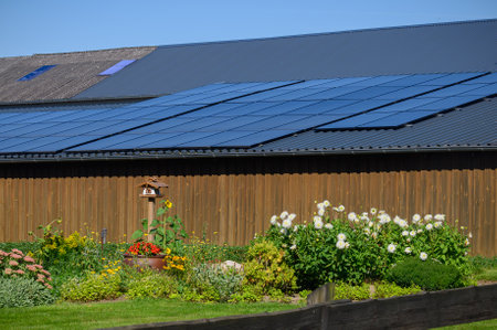 Solar panels situated on the roof of the farm barn with flower garden in the foreground. Solar modules on the barn roof as integration of sustainable technology into agricultural iの写真素材