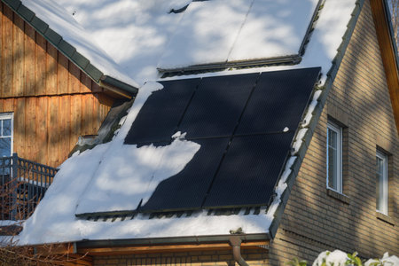Solar water heater and solar power plant on a roof of residential house covered with snow. Solar thermal collector and photovoltaic panels on the roof of house covered with snow.の写真素材