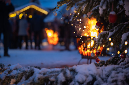 Fir tree branches covered with snow, adorned with sparkling Christmas balls, set against warm glow of a fire pit with delightful bokeh. Scene from Christmas market with snow, Christの写真素材