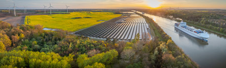 Ground-mounted solar photovoltaic panels, wind turbine farm neighboring canal, where ship gracefully...