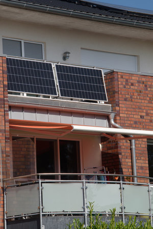 Modern residential building with solar panels on a balcony railing and on roof. Solar panels on balcony, approach of integrating renewable energy sources into urban design to reduceの写真素材