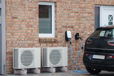 Sustainable living EV charging and heat pumps. Modern home equipped with energy-efficient solutions, including two heat pump units and an electric vehicle (EV) charging station.の写真素材