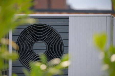 Close-up view of heat pump unit with a circular fan design framed by soft green foliage. Concept engineering of sustainable home heating technology.の写真素材