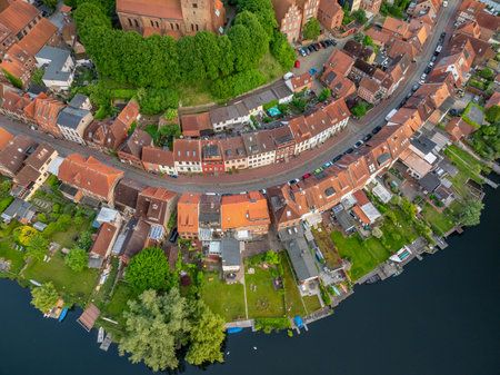 Top-down drone view of historic old town of MÃ¶lln with curved street, red-tiled roofs of houses along waterfront, gardens, small docks, trees and church complex surrounded by greenの写真素材